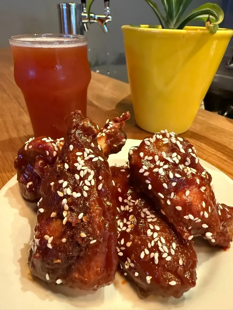 Sticky glazed chicken wings with sesame seeds, beer, and plant.