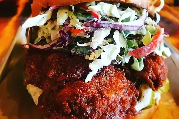 Close-up of a fried chicken sandwich with coleslaw and red onions.
