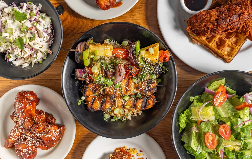 Various dishes: chicken and waffles, coleslaw, wings, salad, and kebabs.