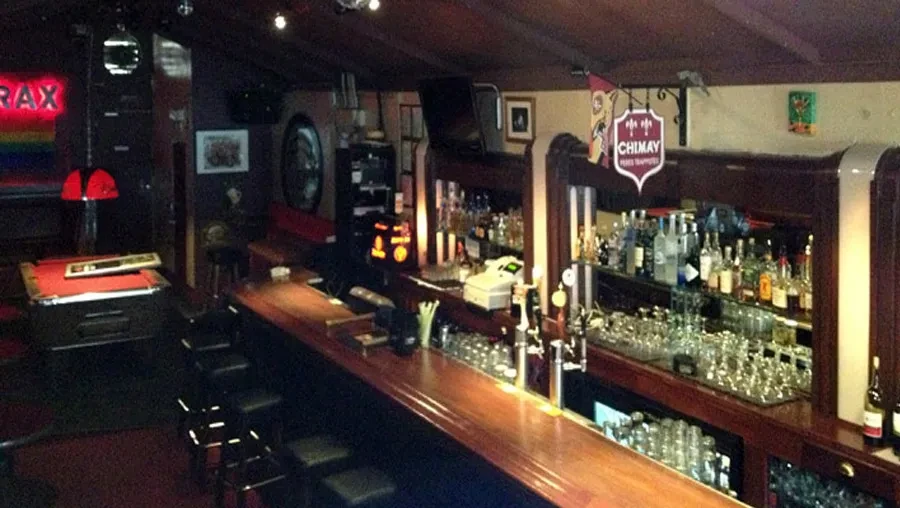 An empty, dimly lit bar with a pool table and barstools.