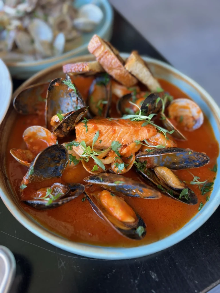 A bowl of seafood stew with salmon, mussels, and clams.