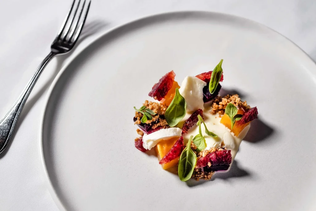 Deconstructed dessert with fruits, cream, crumble, and basil on a white plate.
