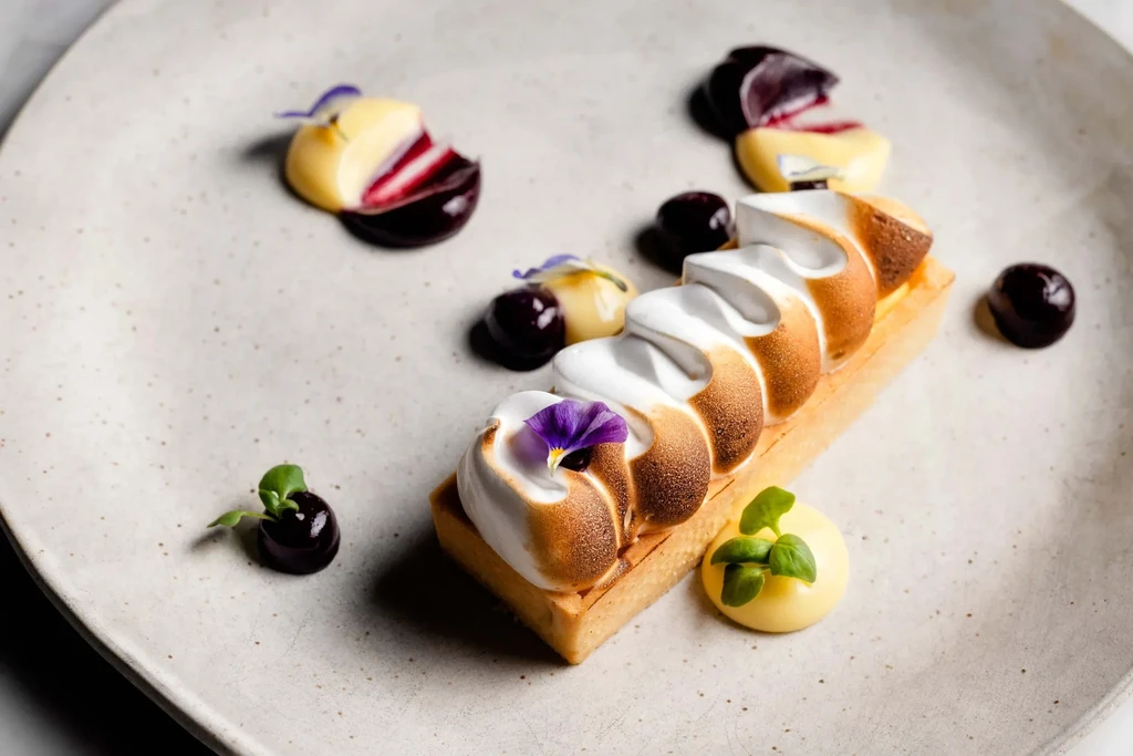 A lemon meringue tart, decorated with purple flowers and small candies.