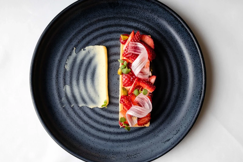 Dessert plate with strawberry tart, cream swirl, and garnishes.