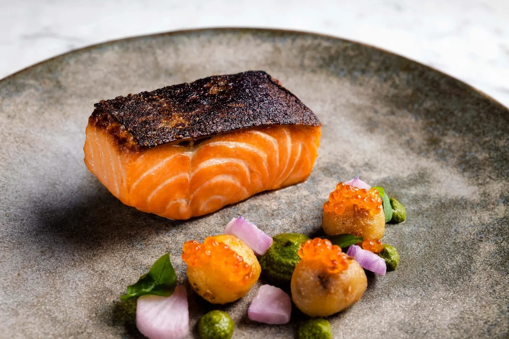 Grilled salmon fillet, new potatoes, caviar, and fresh herbs on a plate.
