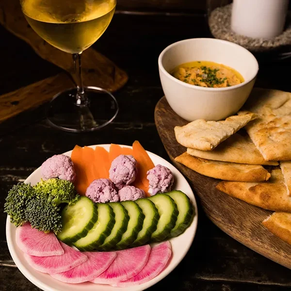 A plate of colorful vegetables, hummus with pita bread, and a glass of wine.