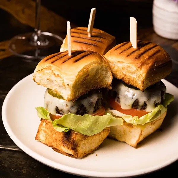 Three small cheeseburger sliders with grilled buns and toothpicks on a plate.