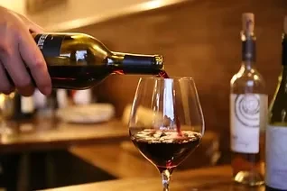A hand pours red wine from a bottle into a clear glass.