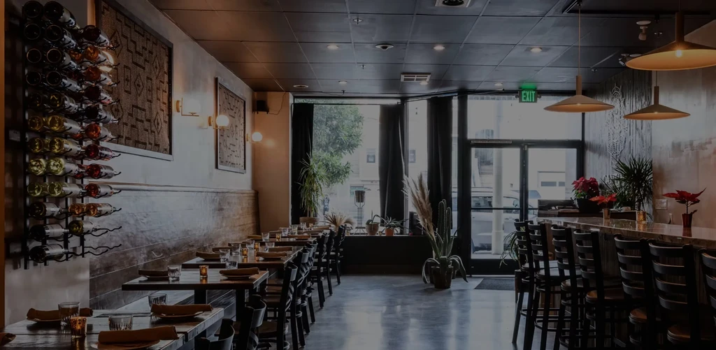 A restaurant with tables, a wine rack, a bar, and an exit sign.