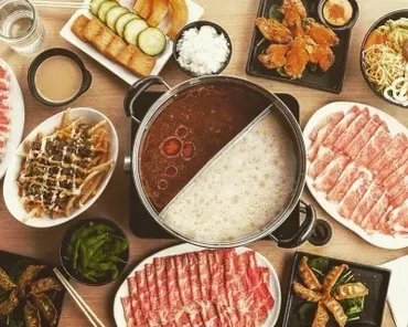 Overhead view of a hot pot with plates of meat, vegetables, and snacks.