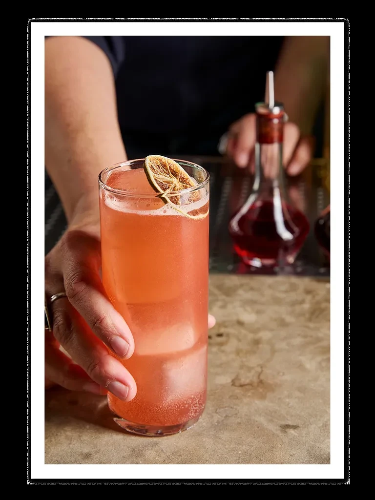 A bartender serving a pink cocktail with a dried lime garnish.