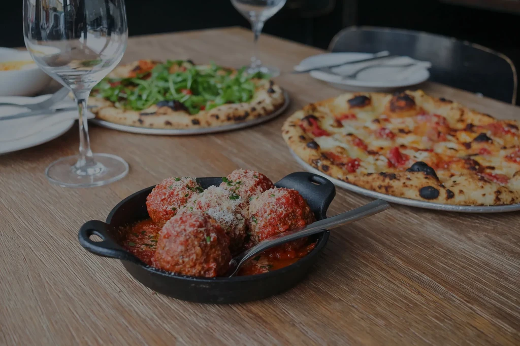 Meatballs in sauce and two pizzas on a wooden table.