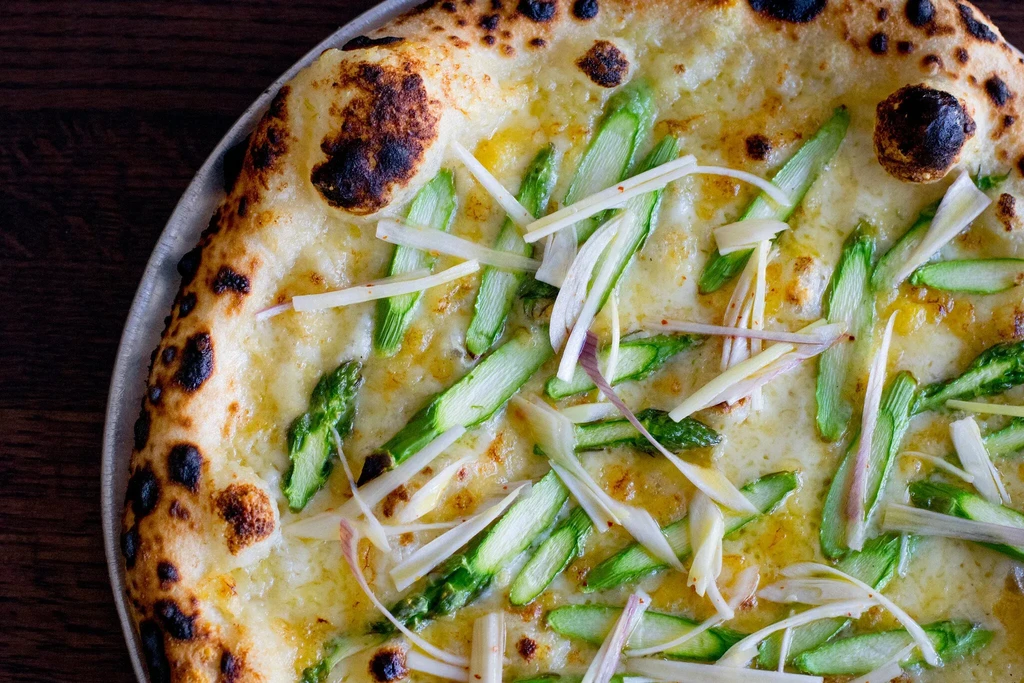 Close-up of a cheese pizza topped with asparagus slices and thin white strips.
