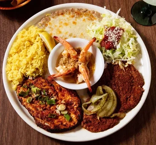 A plate of Mexican food with rice, shrimp, meat, and salad.
