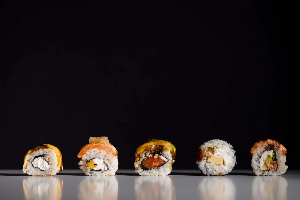 Five assorted sushi rolls on a reflective surface against a black background.