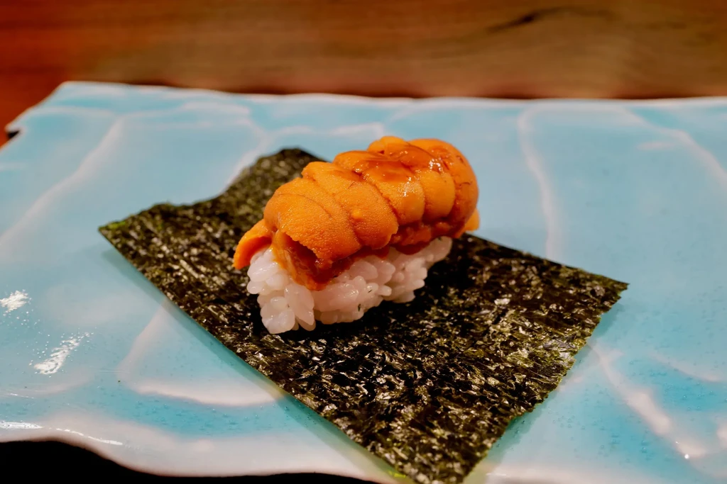 Sea urchin (uni) sushi on seaweed and rice, on a light blue plate.