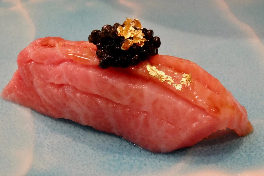 Close-up of a pink fish slice topped with caviar and gold flakes.