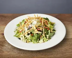 A white plate of salad with lettuce, black beans, cheese, and tortilla strips.