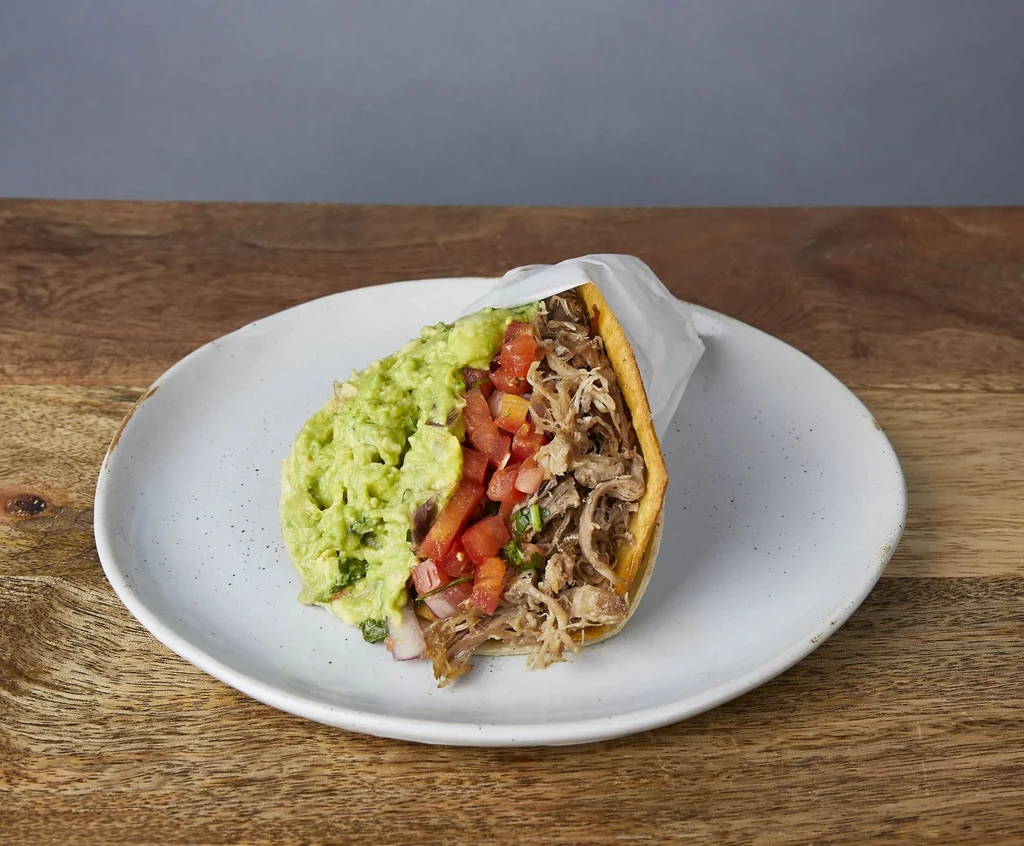 A taco filled with guacamole, diced tomatoes, and shredded meat.