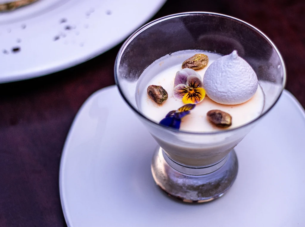 Panna cotta dessert in a glass, garnished with flowers and pistachios.