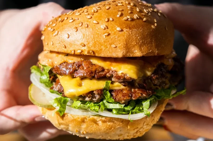 Close-up of a person holding a double cheeseburger.