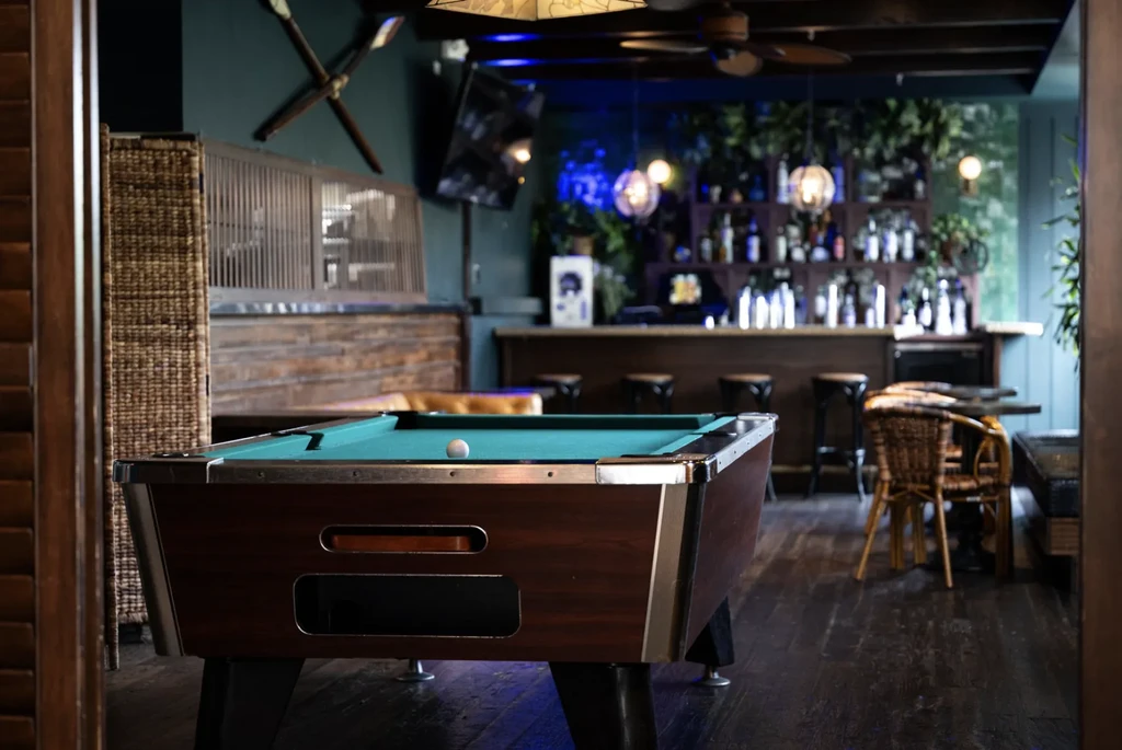 A pool table with a cue ball in a dimly lit barroom.