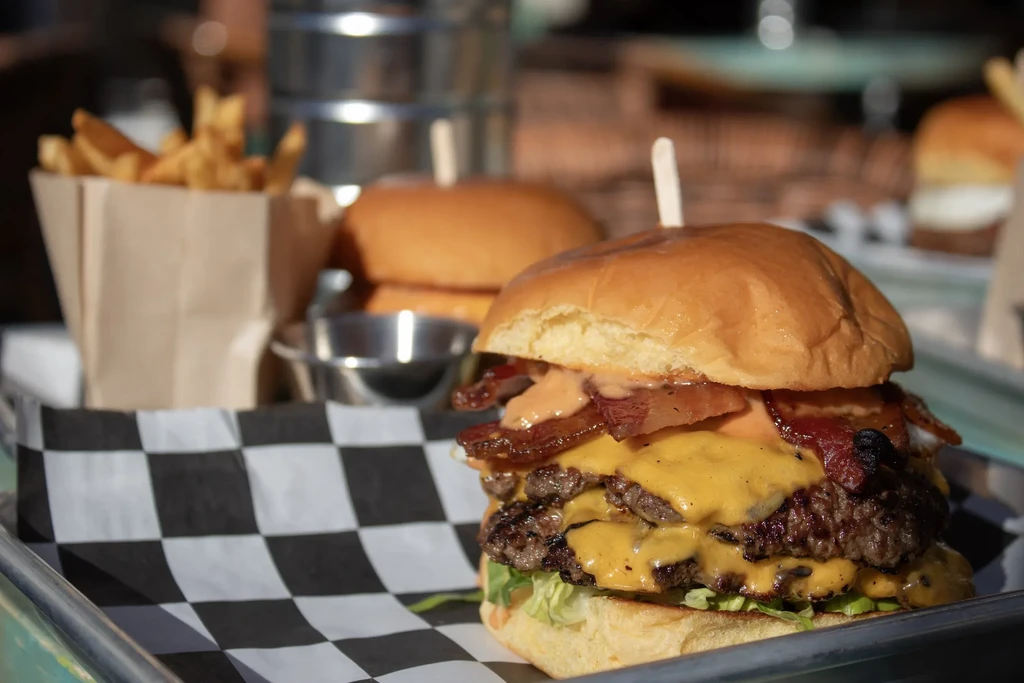 A double cheeseburger with bacon and fries on a checkered paper-lined tray.