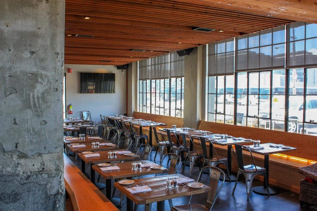 An empty modern restaurant with industrial windows and rustic wooden tables.