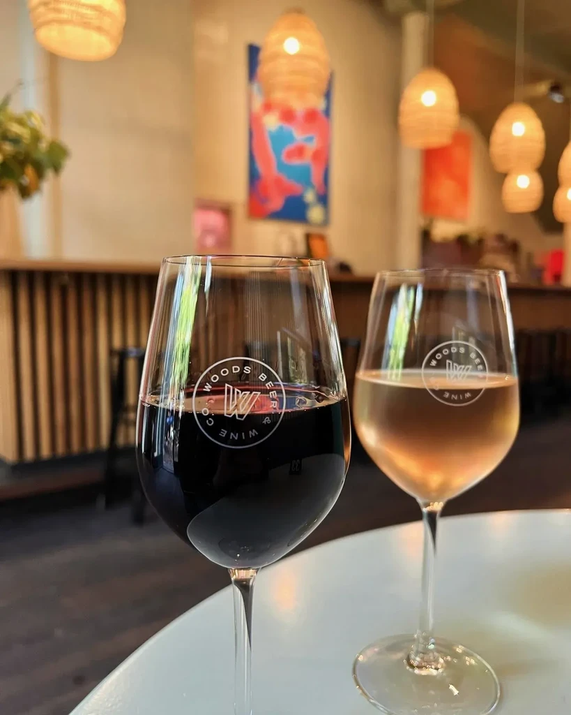 Two "Woods Beer & Wine Co" branded wine glasses with red and white wine.