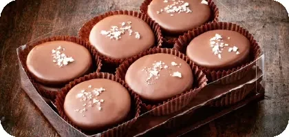 Six round milk chocolate candies with sea salt flakes in a box.
