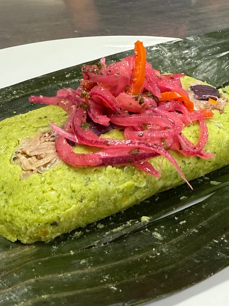A green tamale with meat filling, topped with pickled red onions.
