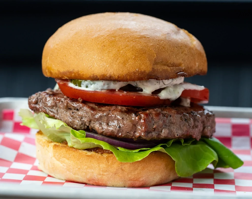 A close-up of a burger with a patty, lettuce, tomato, and sauce.