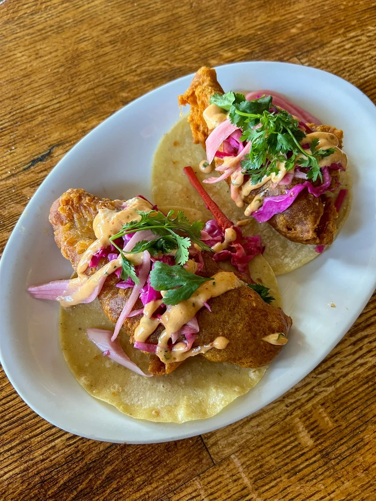 Two crispy fried fish tacos with pink cabbage, cilantro, and sauce.