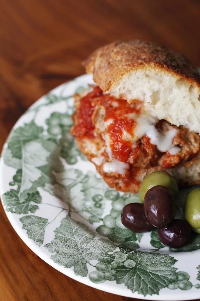 Meatball sub with melted cheese, marinara sauce, and olives on a plate.