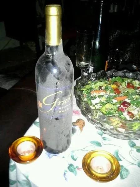 Wine bottle, salad, and candles on a floral tablecloth.