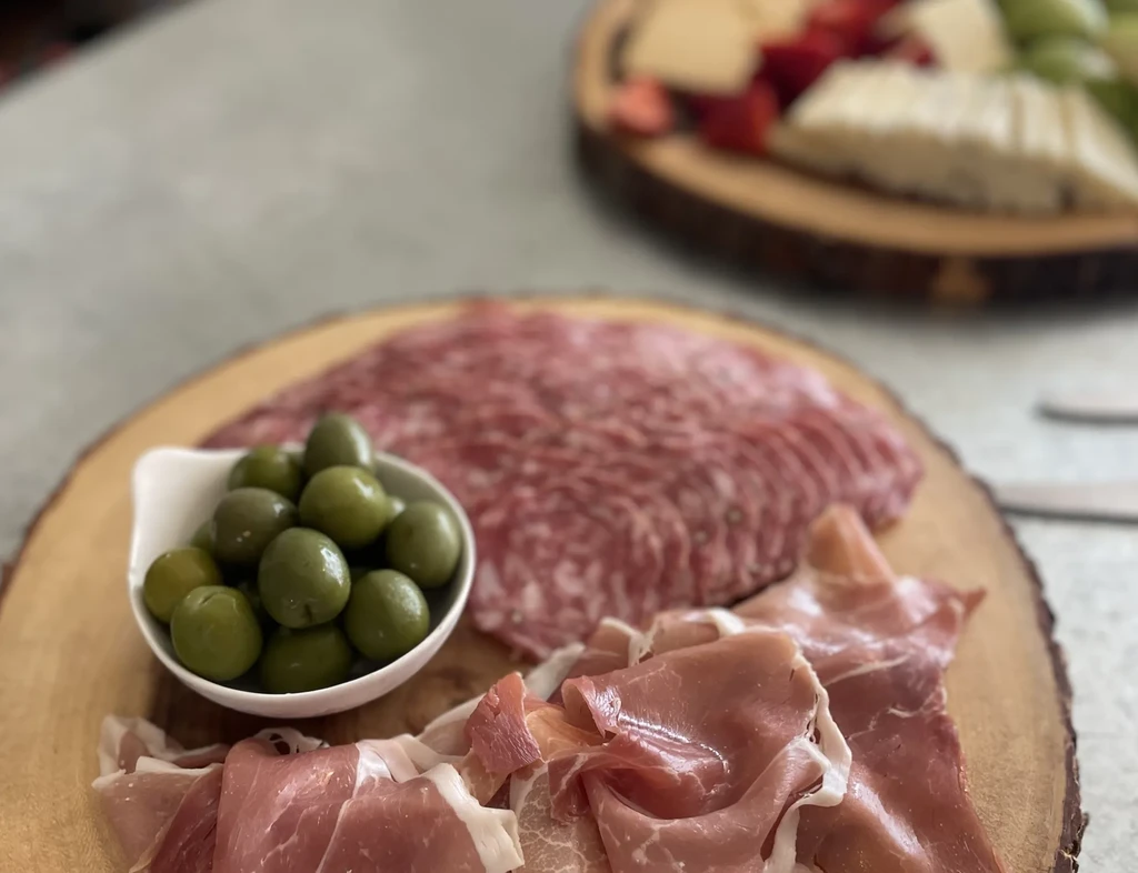 A charcuterie board with olives, salami, and prosciutto on a wooden platter.