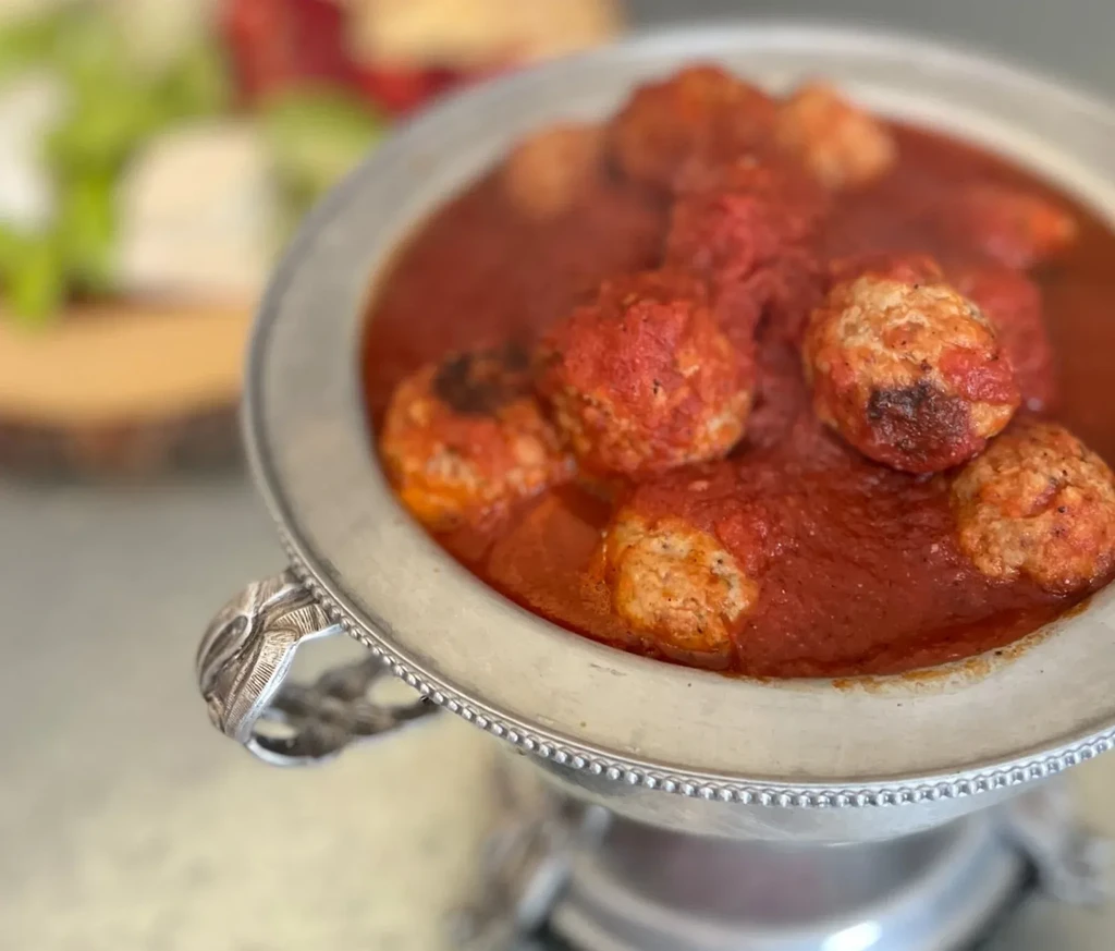 Meatballs covered in red sauce in a decorative silver serving bowl.
