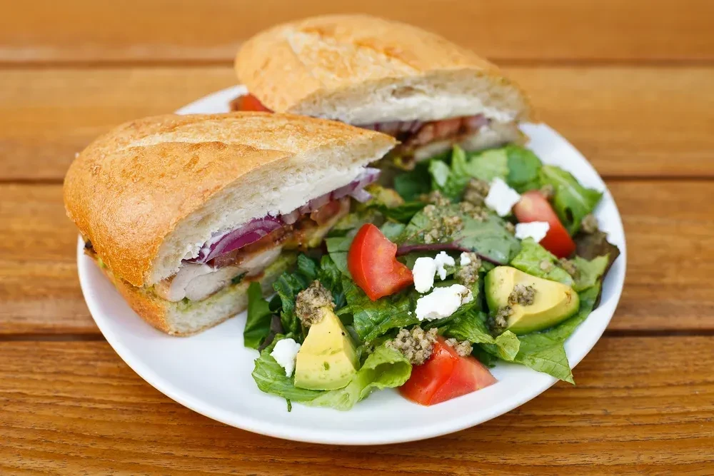 Half chicken sandwich with red onion and a green salad.
