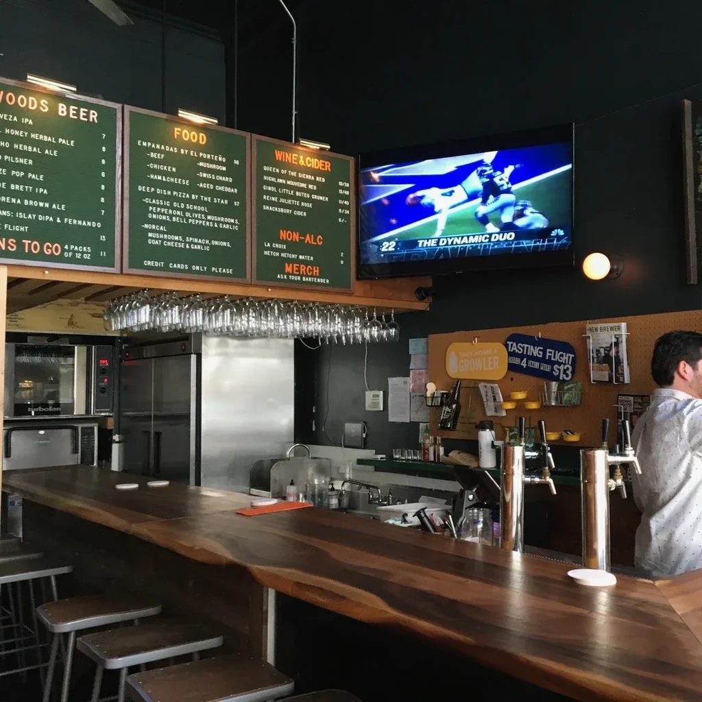 A modern bar with a wooden counter, bar stools, and menu boards.