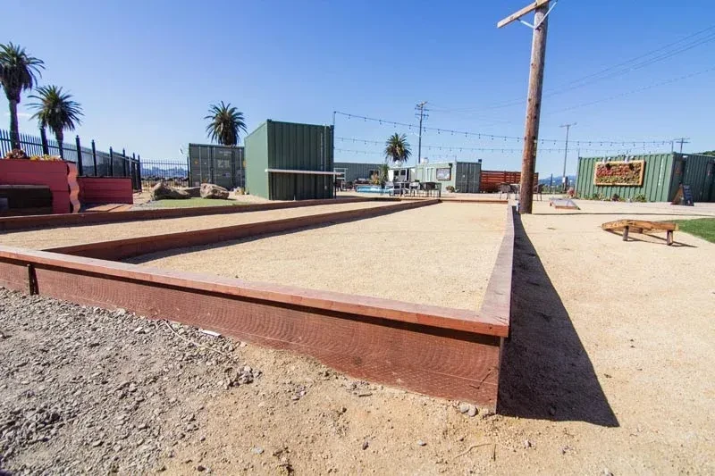 Two empty bocce ball courts and cornhole sets on a sunny day.
