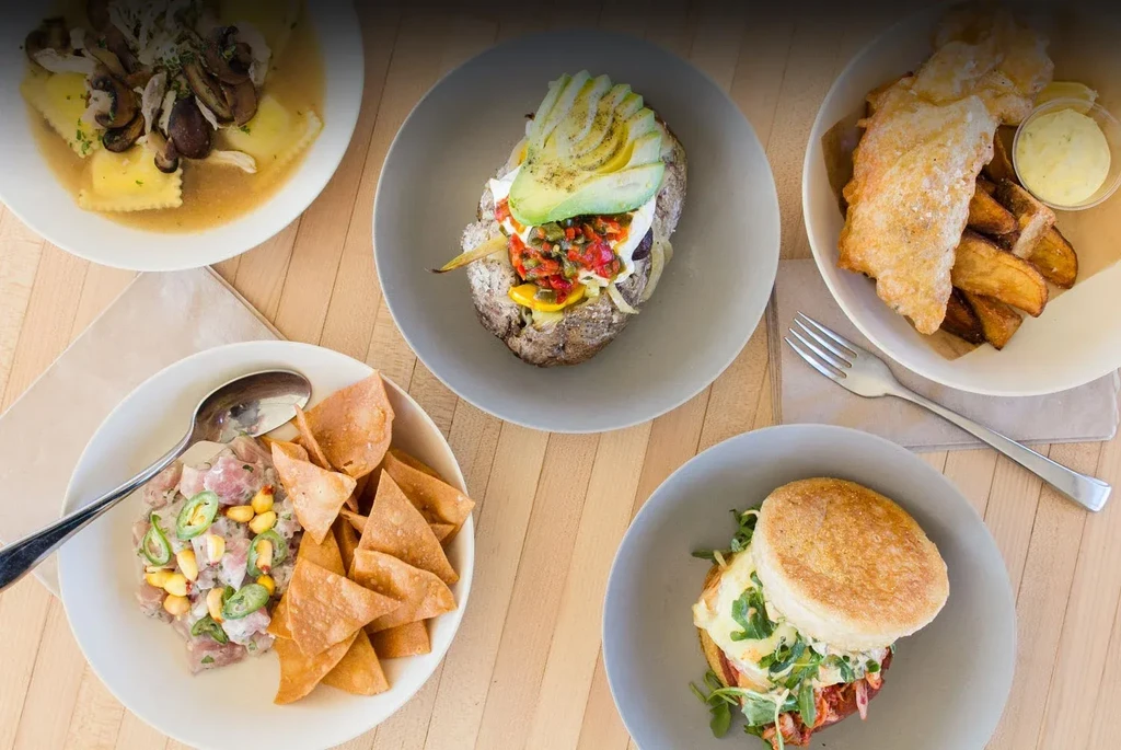 A top-down view of five diverse food dishes on a wooden table.