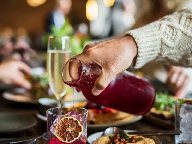 A person pours red juice into a glass at a dinner table.