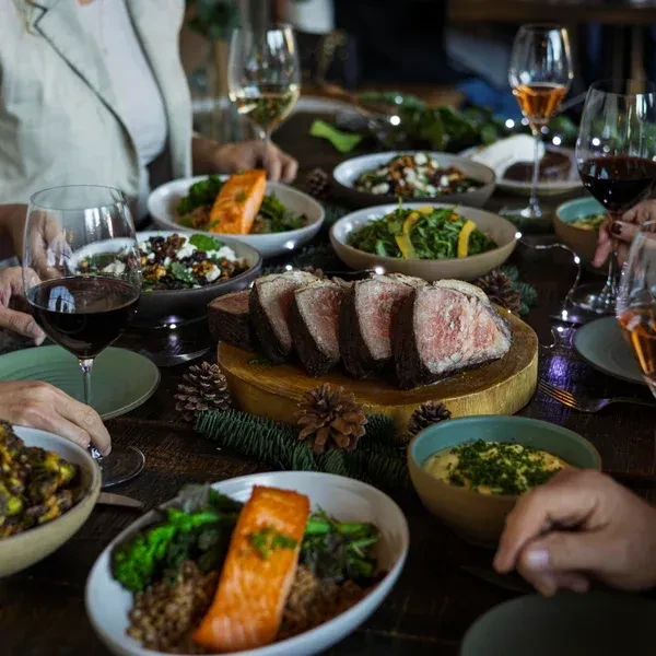 A holiday meal with sliced roast beef, salmon, salads, and wine.