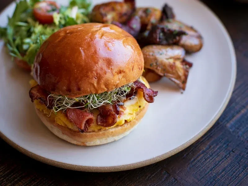 Breakfast sandwich with bacon, eggs, sprouts, and roasted potatoes.