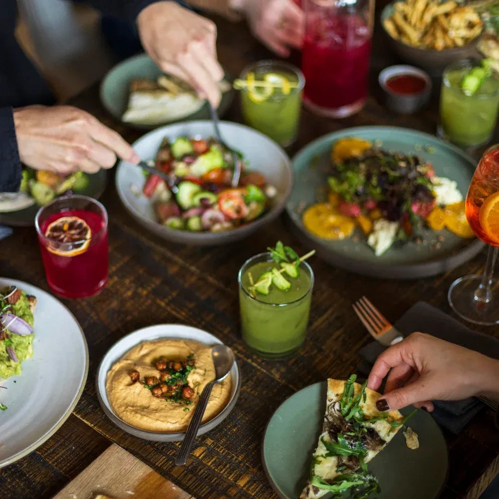 A table with multiple hands serving and eating a variety of healthy foods.