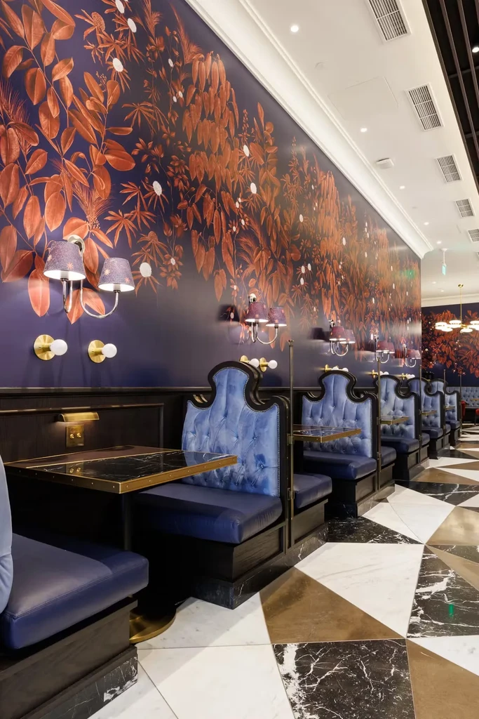 A long wall with dark floral wallpaper and blue booths in a restaurant.
