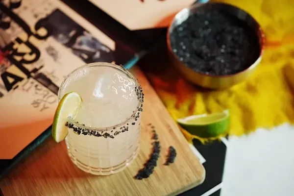 A lime margarita with black salt rim and a bowl of black salt.
