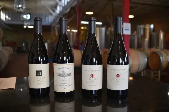 Four bottles of Pinot Noir wine on a dark table.