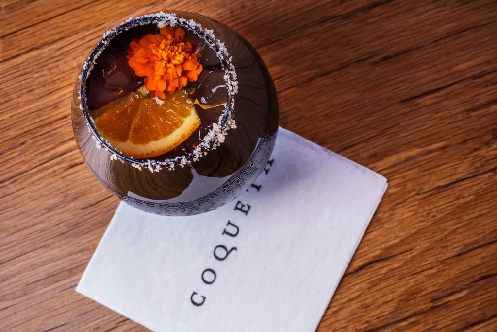Dark drink with orange slice and orange flower in a glass.