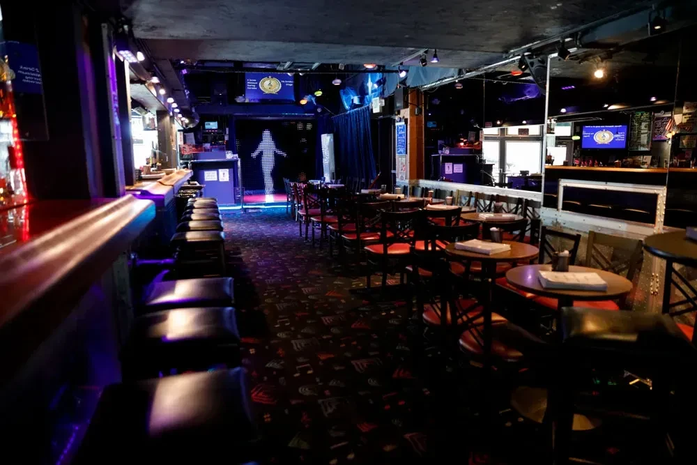 An empty, dimly lit bar with a stage, tables, and a bar counter.